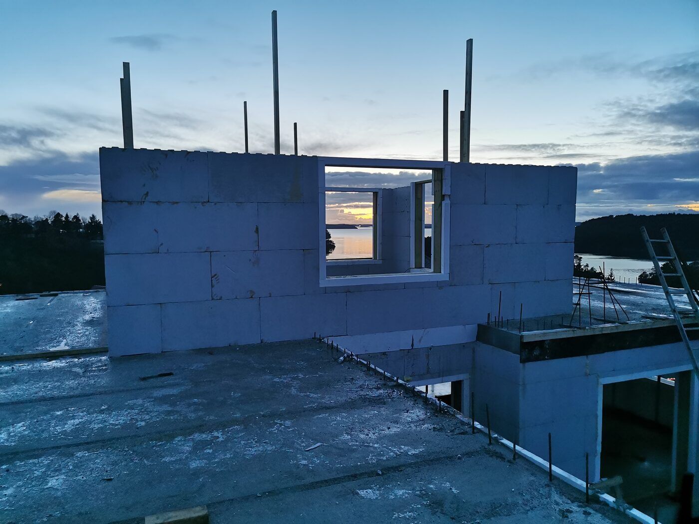 Penthouse-etasjen under oppføring med stor vindusåpning som rammer inn solnedgang over fjorden mot vest