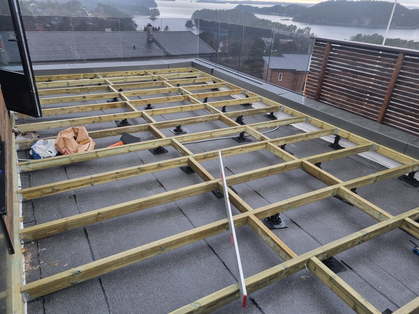 Takterrasse med bjelkelag og glassrekkverk under ferdigstillelse, utsikt mot øyer og sjø