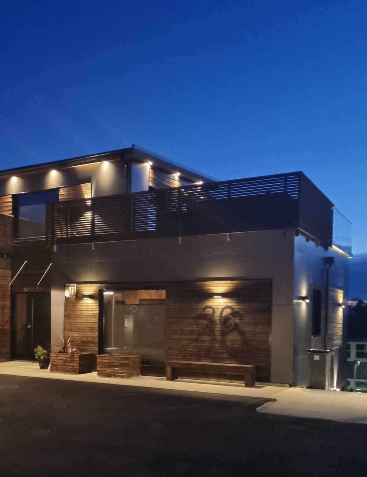 Inngangsparti i blåtimen med varm fasadebelysning, takterrasse og husnummer 36 på veggen
